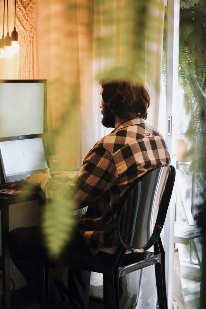 Person som sitter vid datorn, grönska i förgrunden.