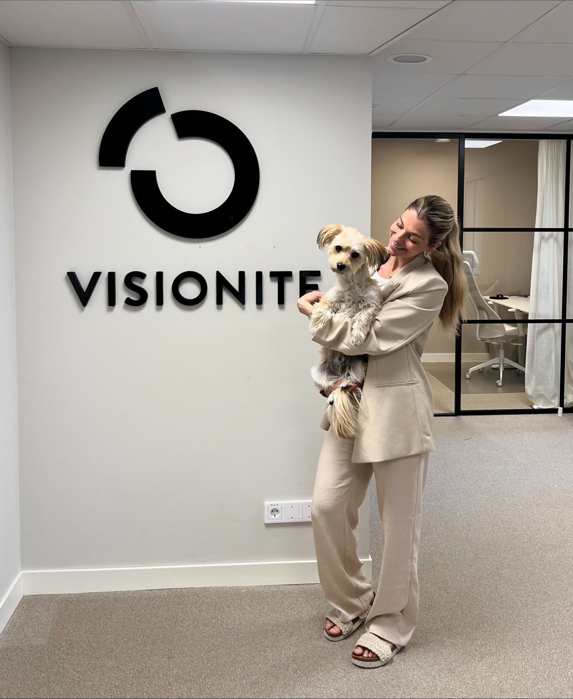 Kvinna håller i en hund framför Visionite-skylt