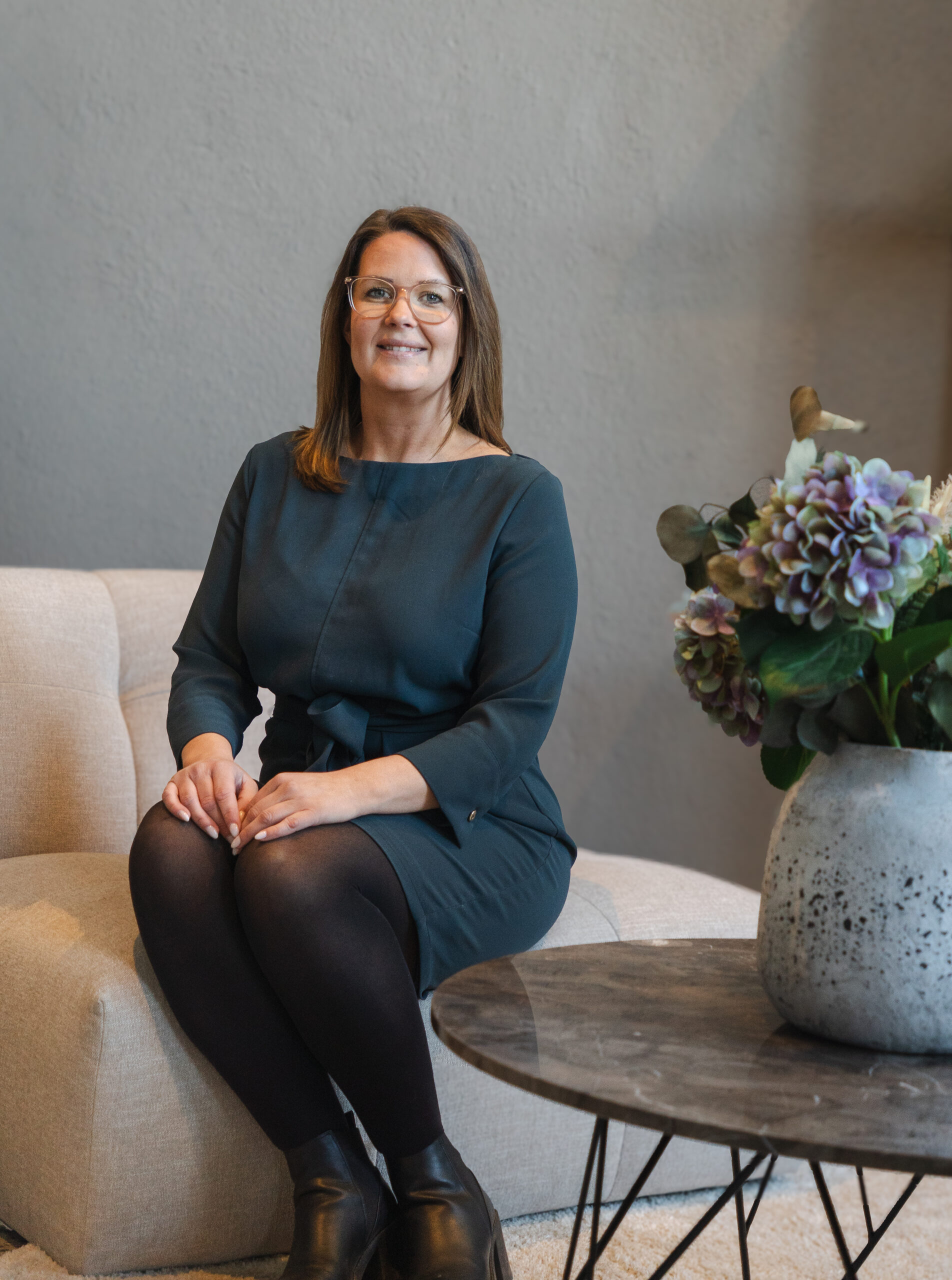 Sara Engström, VD Visionite Skellefteå, Umeå och Örnsköldsvik, sitter på en beige fåtölj med händerna i knät och ler mot kameran. Hon har på sig en mörkgrön klänning, bredvid henne står ett runt bort med en stor blomma på.